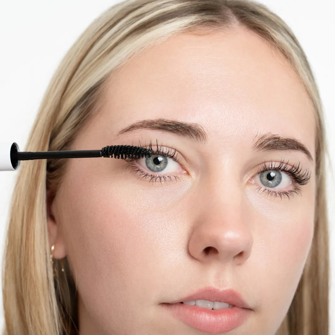 Woman applying mascara to her eyelashes with a close-up of the brush.