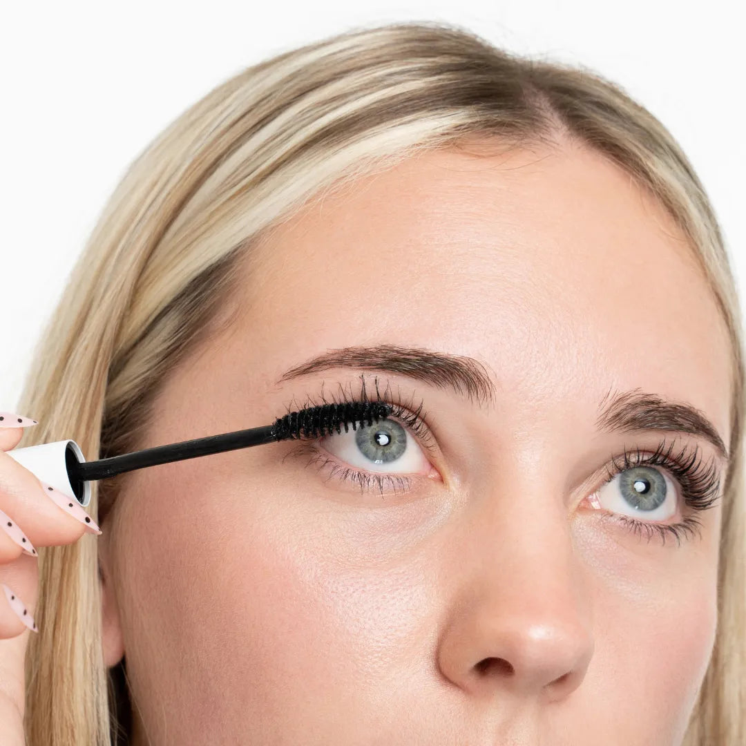 Woman applying mascara to her eyelashes with a white background