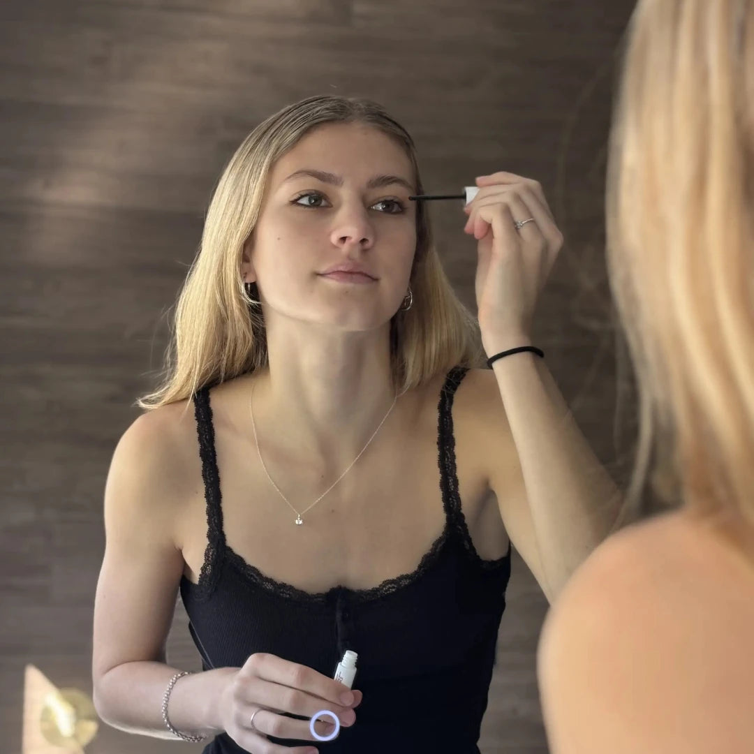 woman applying lash serum in front of mirror