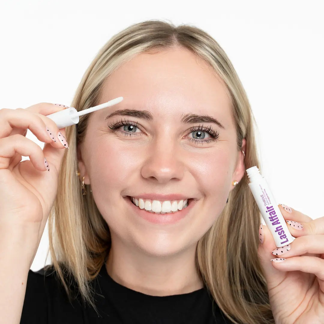 woman applying  a brow serum while holding the tube in other hand